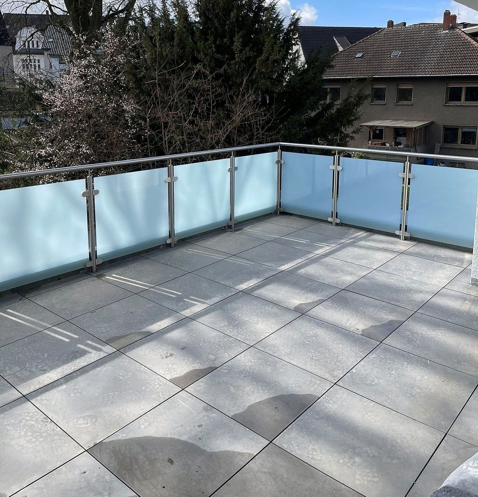 Balkongeländer aus Edelstahl mit Milchglasfüllung auf einem gefliesten Balkon